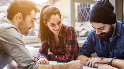 Drei Personen sitzen an einem Tisch und arbeiten gemeinsam.